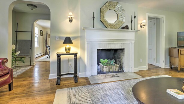 A living room with hardwood floors, a fireplace, a round coffee table, and a red leather chair. - Historic Essex Home w/ Large Yard Near Downtown! (Essex)