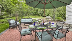 An outdoor patio with a table set for four, surrounded by chairs and a large umbrella. - Historic Essex Home w/ Large Yard Near Downtown! (Essex)