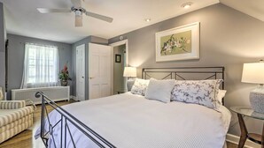 A bedroom with a bed, a ceiling fan, a window with curtains, a radiator, a chair, and a framed picture on the wall. - Historic Essex Home w/ Large Yard Near Downtown! (Essex)