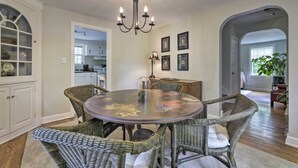A dining area with a round table, wicker chairs, a chandelier, and framed pictures on the wall. - Historic Essex Home w/ Large Yard Near Downtown! (Essex)