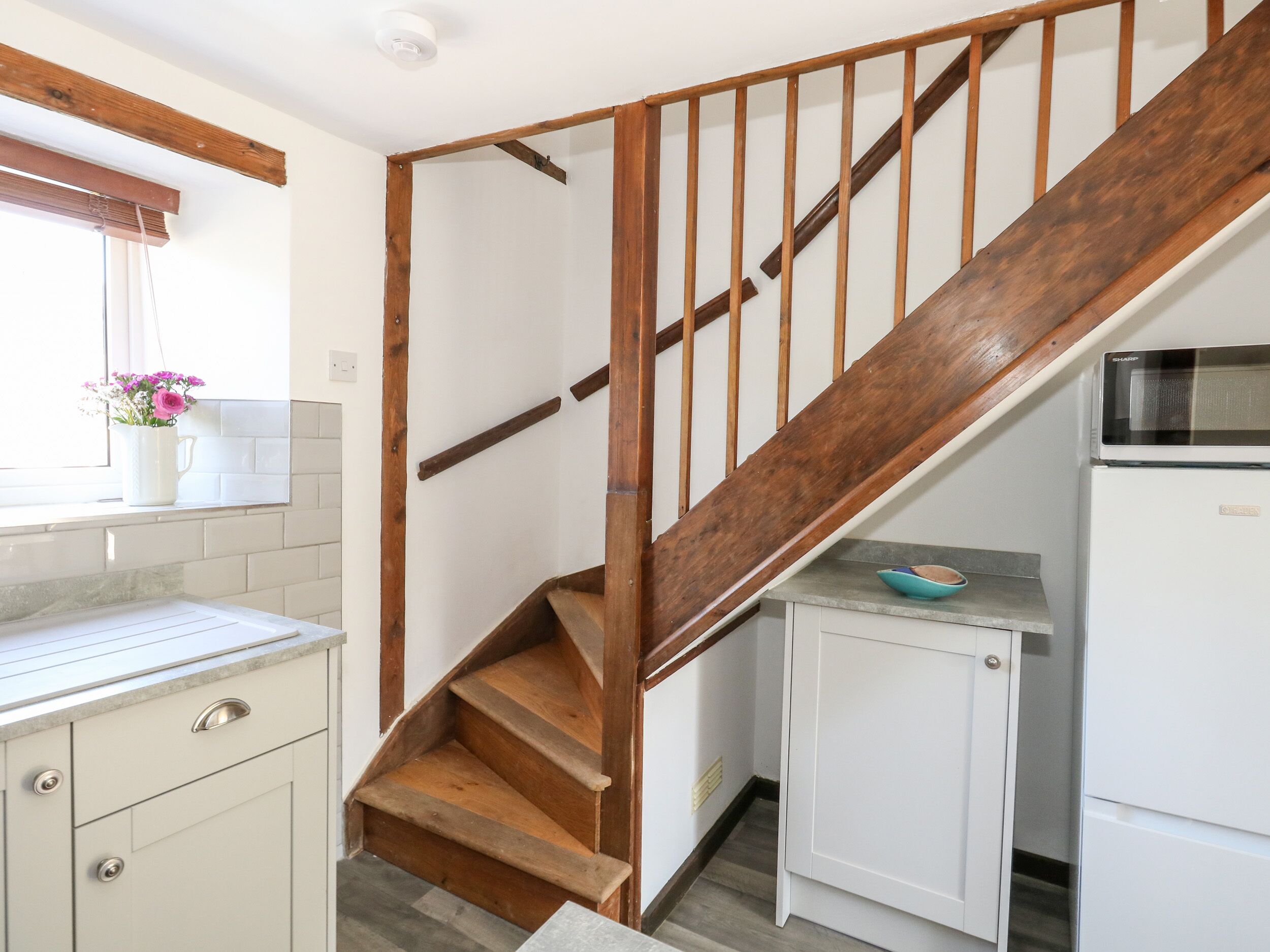 Eine Küche mit einer Holztreppe, weißen Schränken und einer Mikrowelle.
