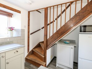 A kitchen with a wooden staircase, white cabinets, and a microwave. - Tiddlers Cottage (Bridport)