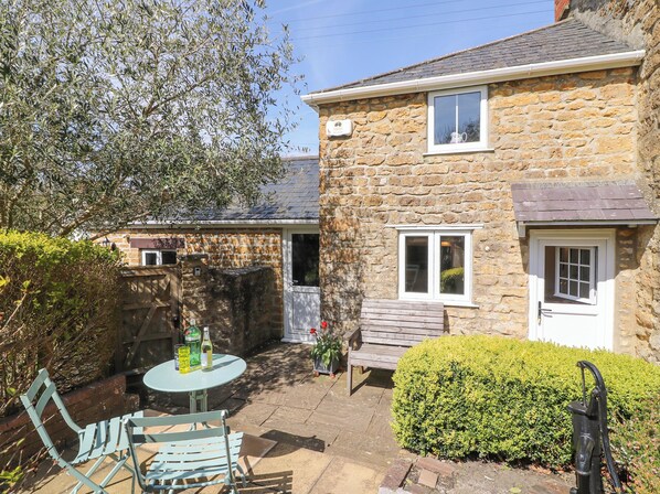 A stone house with a patio, a table with chairs, and a small garden. - Tiddlers Cottage (Bridport)