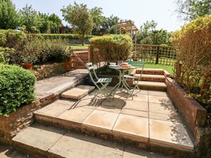 A patio area with a table and chairs, surrounded by a brick wall and greenery. - Tiddlers Cottage (Bridport)