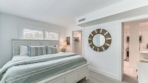 A bedroom with a bed, a round mirror, and a view into the bathroom. - Coastal Downtown Naples Condo - Walk to the Beach! (Naples)