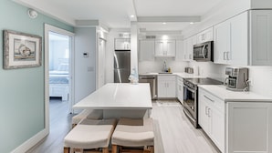 A modern kitchen with white cabinetry, stainless steel appliances, and a central island with seating. - Coastal Downtown Naples Condo - Walk to the Beach! (Naples)