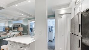 A modern kitchen with white cabinetry, a large stainless steel refrigerator, and a dining area with a white table and chairs. - Coastal Downtown Naples Condo - Walk to the Beach! (Naples)