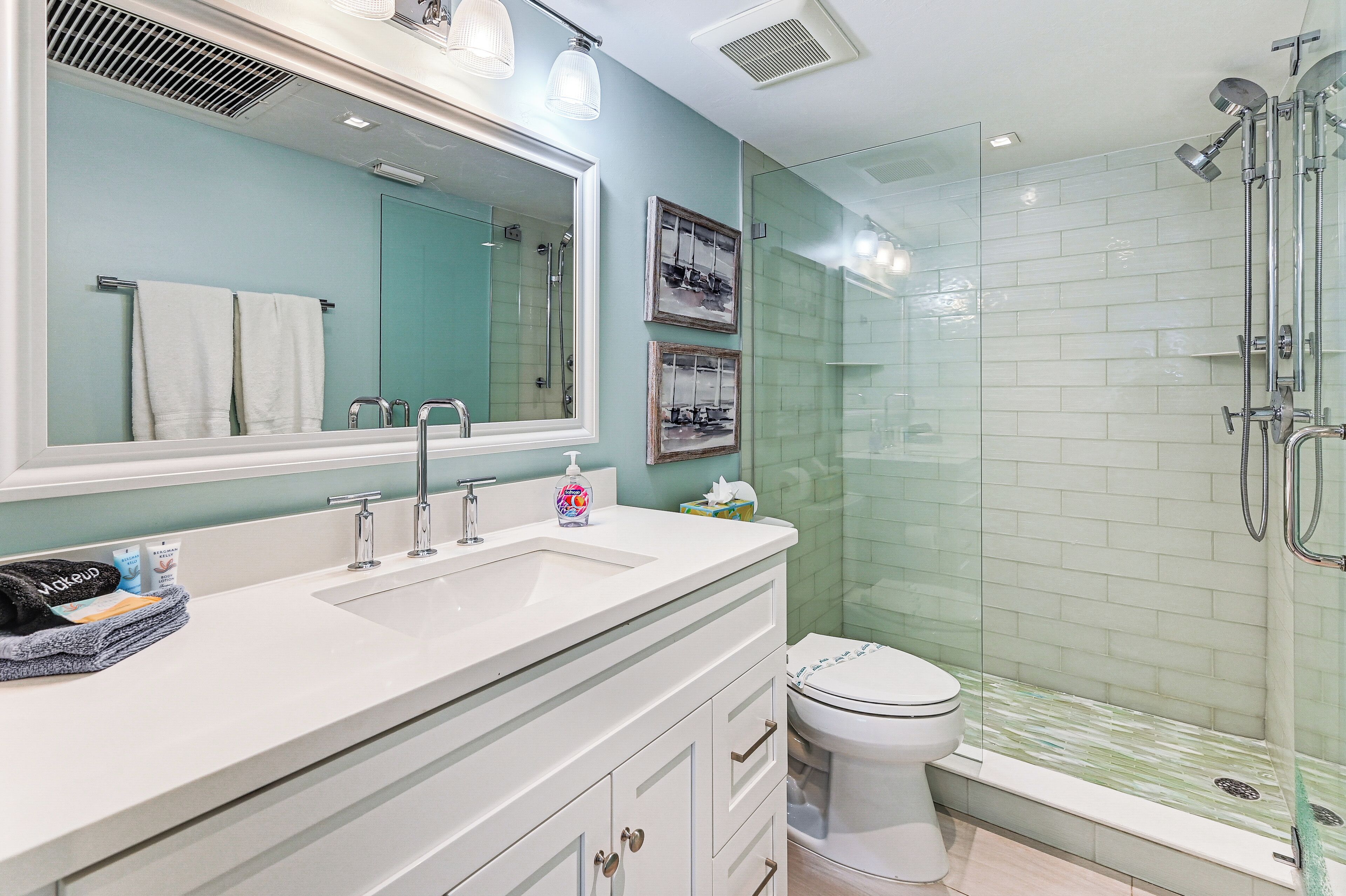 A bathroom with a white vanity, a large mirror, a glass shower enclosure, and a toilet.