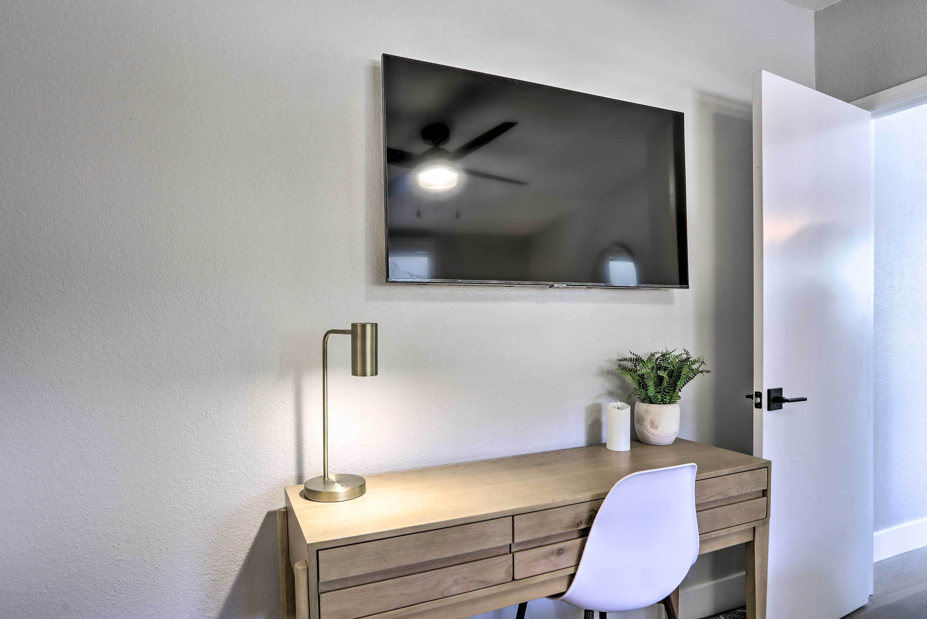 Une pièce comprenant un bureau, une chaise, un téléviseur à écran plat fixé au mur, un ventilateur de plafond et une porte.