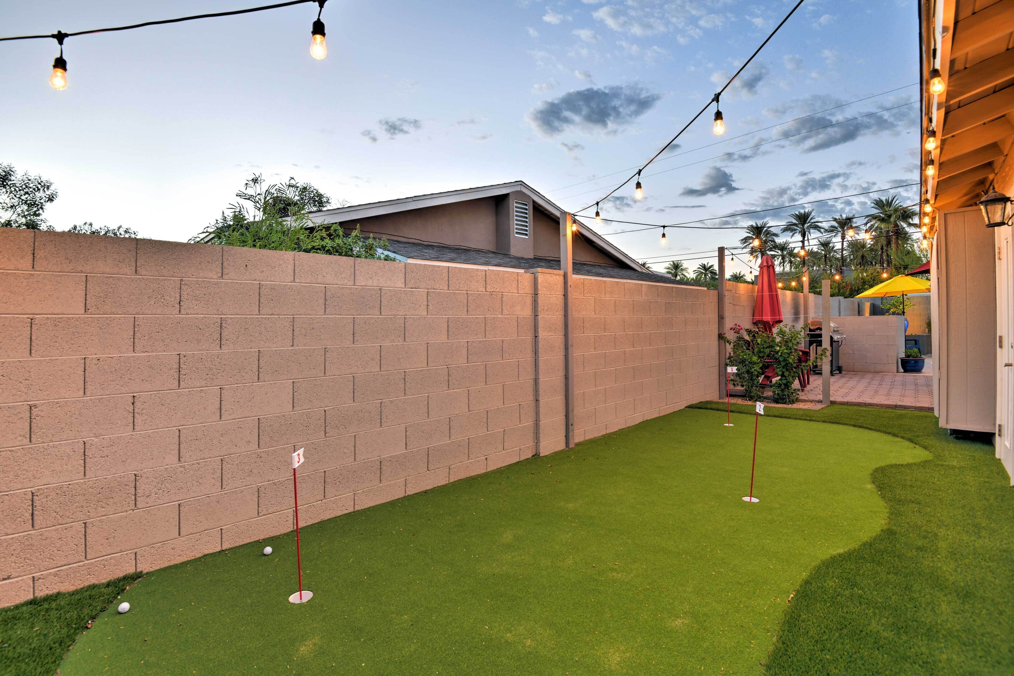A backyard with artificial grass, a brick wall, and string lights.