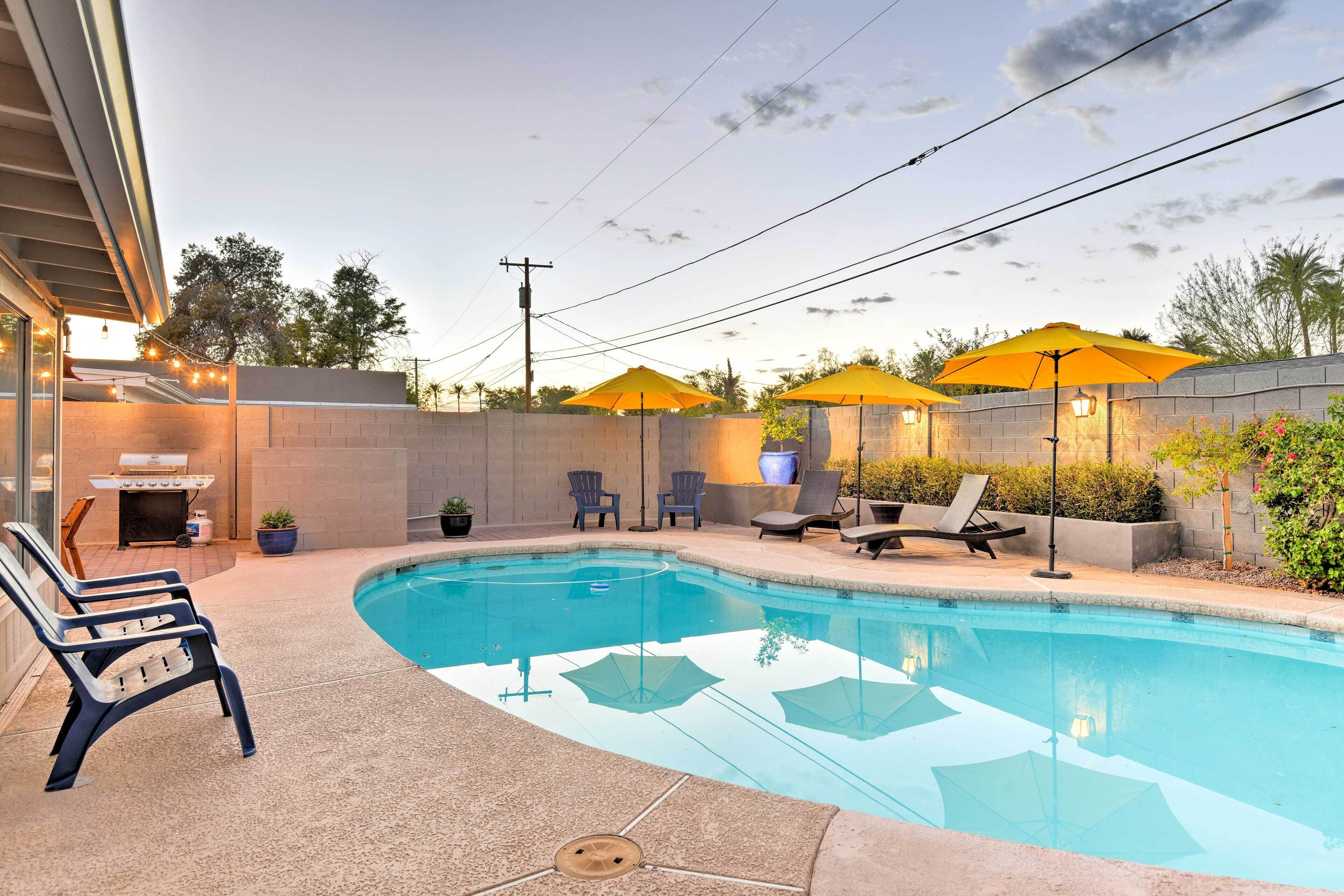A swimming pool with lounge chairs and umbrellas, surrounded by a brick wall and vegetation.
