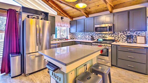 A modern kitchen with stainless steel appliances, a large island, and a wooden ceiling.