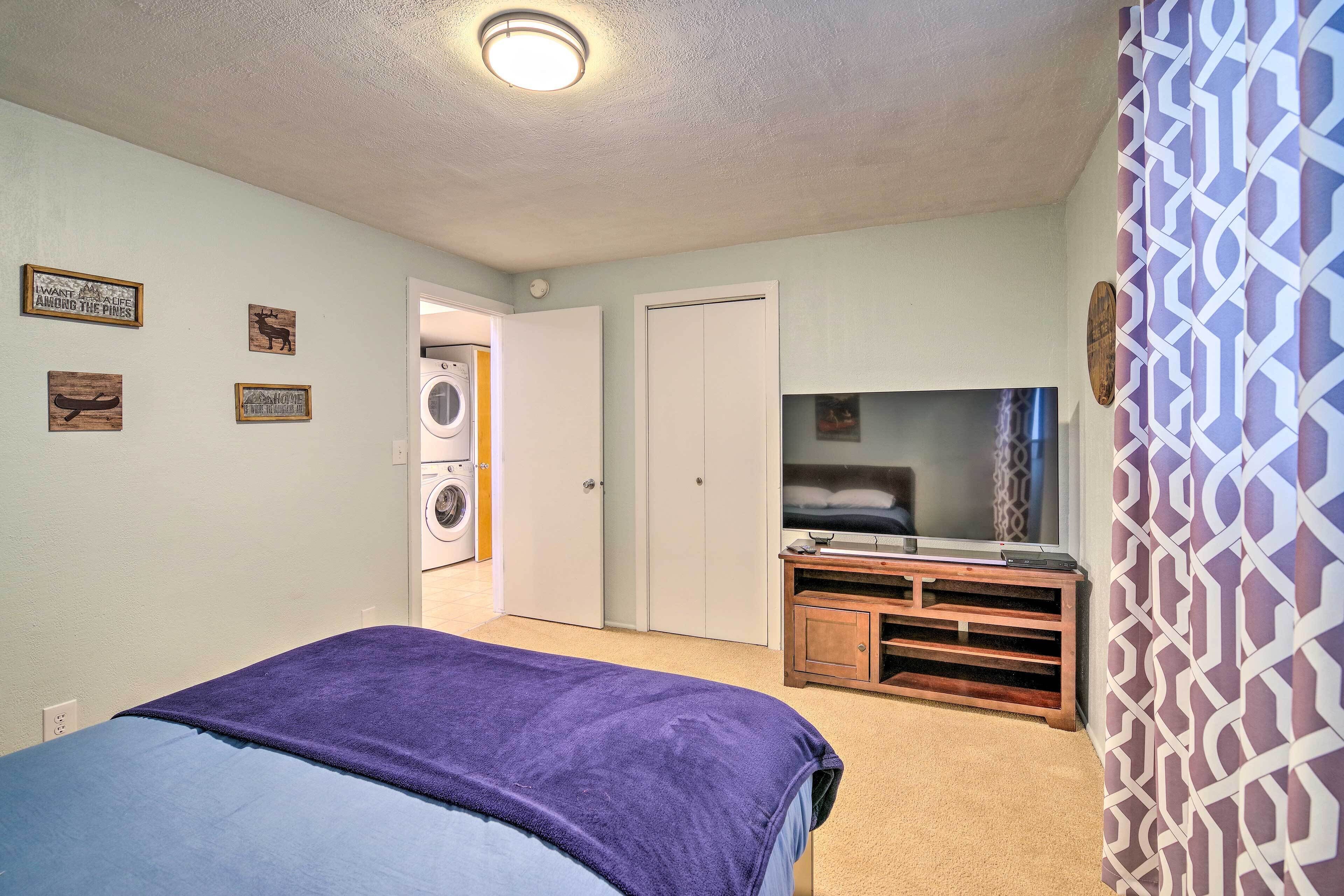 A bedroom with a bed, a washing machine, a TV, and a patterned curtain.