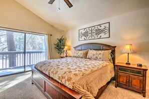 A bedroom with a large bed, a nightstand, a lamp, and a view of trees through a sliding door. - Steps to Golf Course: Condo w/ Grill in Pinetop! (Pinetop)