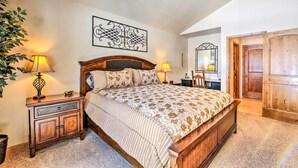Une chambre à coucher avec un lit en bois, deux tables de chevet avec des lampes, un grand miroir et une porte donnant sur une autre pièce.