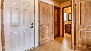 Un couloir avec des portes blanches et en bois, qui mène à une salle de bain équipée d’un lavabo et d’un miroir.