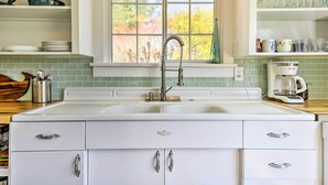 A kitchen with white cabinets, a double sink, and a window with a view of trees.