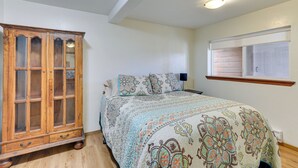 A bedroom with a wooden cabinet, a bed with patterned bedding, a nightstand, and a window with blinds. - Mckinleyville Getaway w/ Hot Tub & Ocean Views! (McKinleyville)