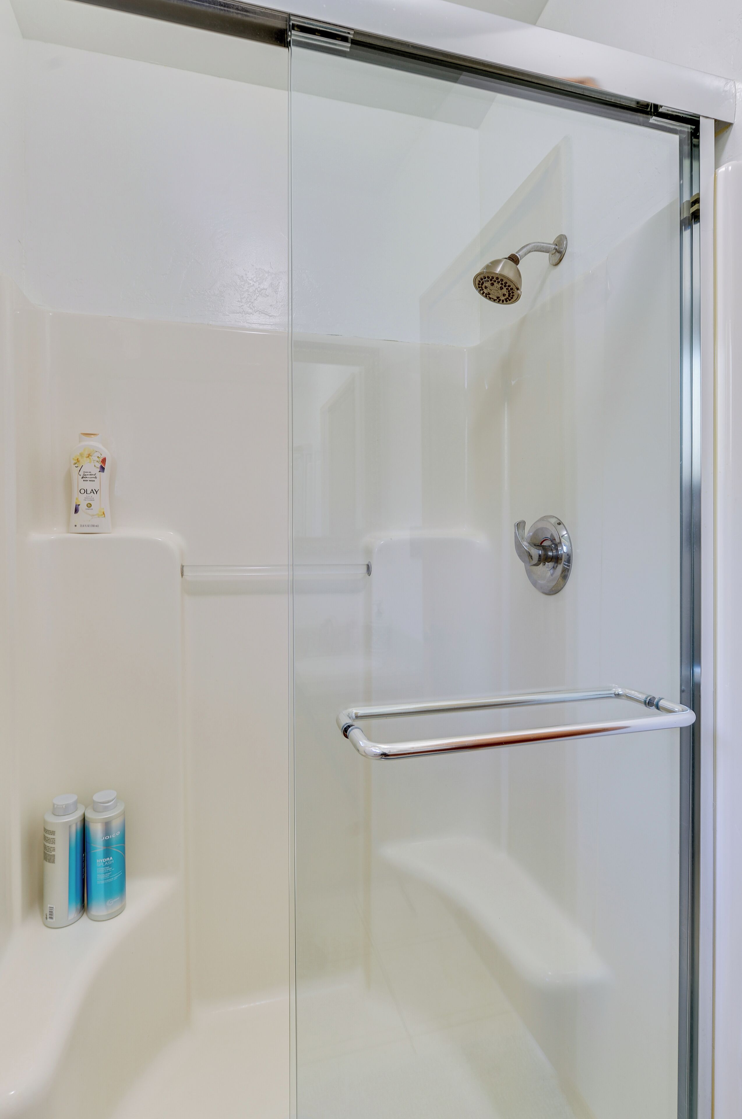 Une douche fermée par des parois de verre, dotée d’un pommeau de douche à main, d’une porte en verre et d’un porte-serviettes.