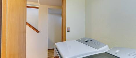 A laundry room with a front-loading washer and dryer, wooden flooring, and a door leading to another room.
