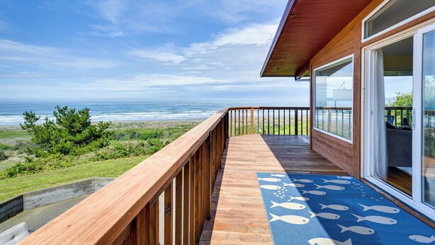 A wooden deck with a view of the ocean, a blue mat with fish patterns, and a railing. - Mckinleyville Getaway w/ Hot Tub & Ocean Views! (McKinleyville)