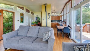 A spacious living area with a grey sofa, a dining table with chairs, and a kitchen in the background. - Mckinleyville Getaway w/ Hot Tub & Ocean Views! (McKinleyville)