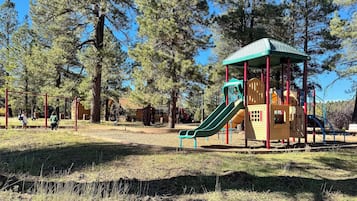 Un parque infantil con un tobogán verde y una casita amarilla.