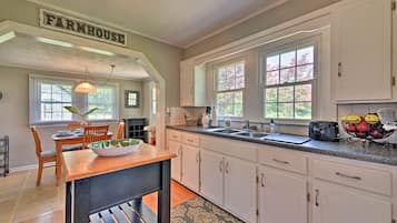 A kitchen with white cabinets, a wooden table, and a farmhouse sign.