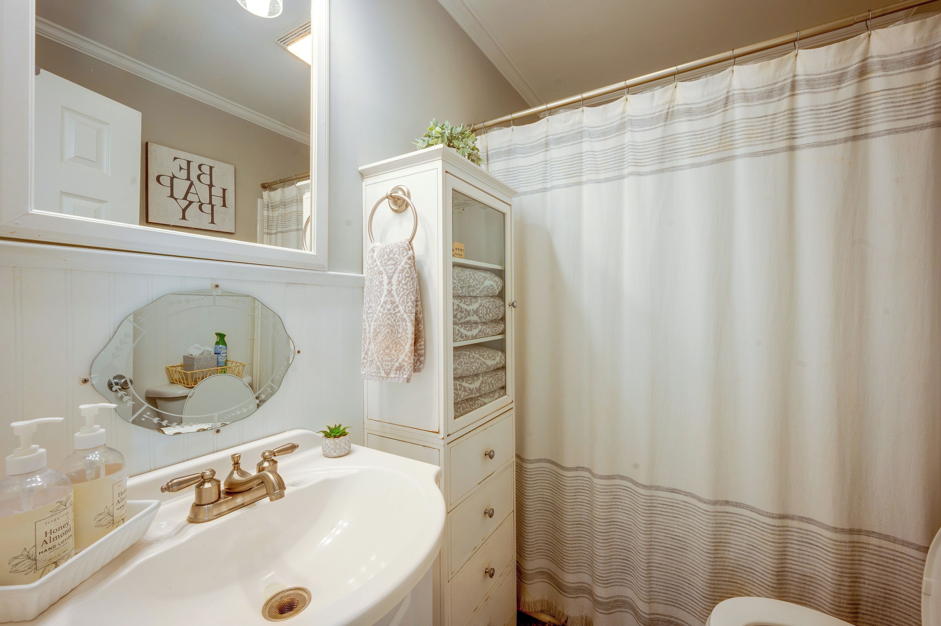 A bathroom with a white sink, gold faucets, a mirror, a towel rack, and a shower curtain.