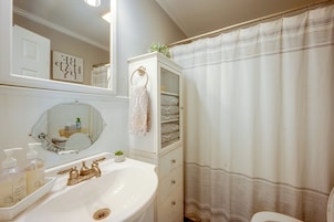 A bathroom with a white sink, gold faucets, a mirror, a towel rack, and a shower curtain.
