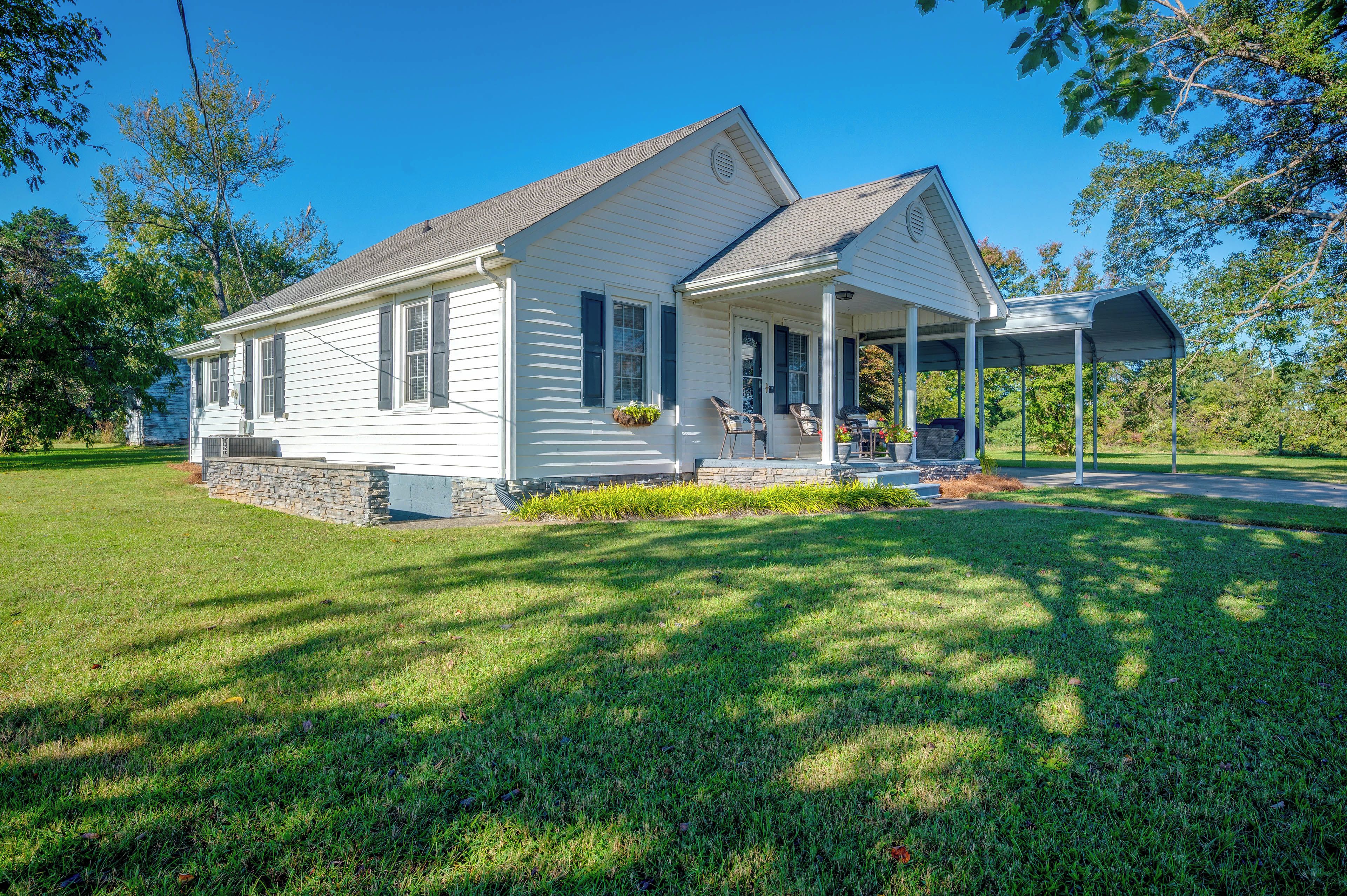 A single-story house with a porch, stone foundation, and a well-maintained lawn.