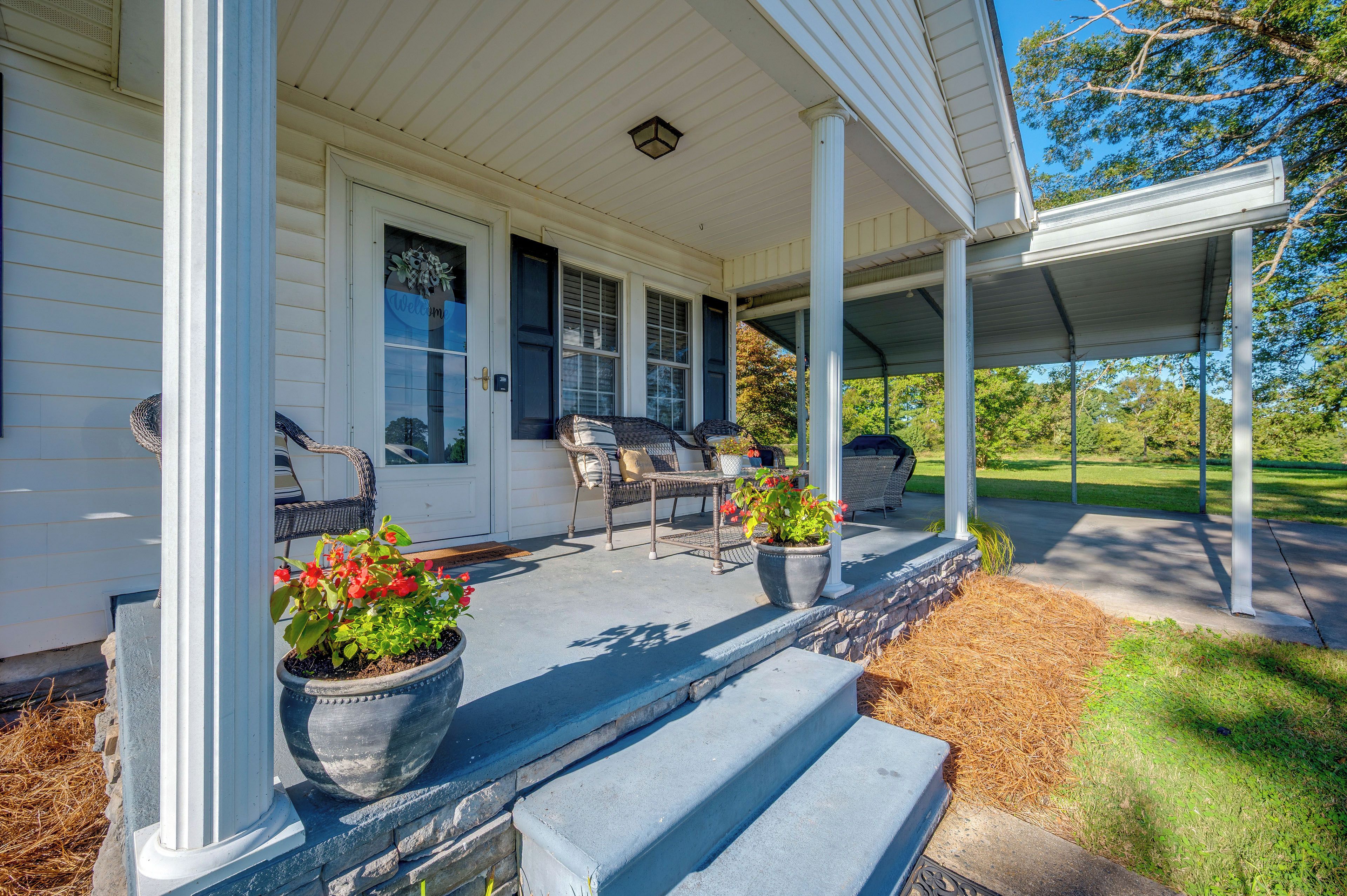 A covered porch with outdoor seating, a welcome mat, and potted plants.