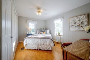 A bedroom with a bed, bedside tables, a chair, a ceiling fan, and a window with curtains.