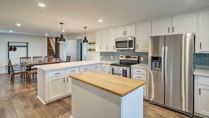 A modern kitchen with white cabinets, stainless steel appliances, and a wooden island. - Fire Pit, Pickleball, Pool! Schulenburg Farmhouse (Schulenburg)
