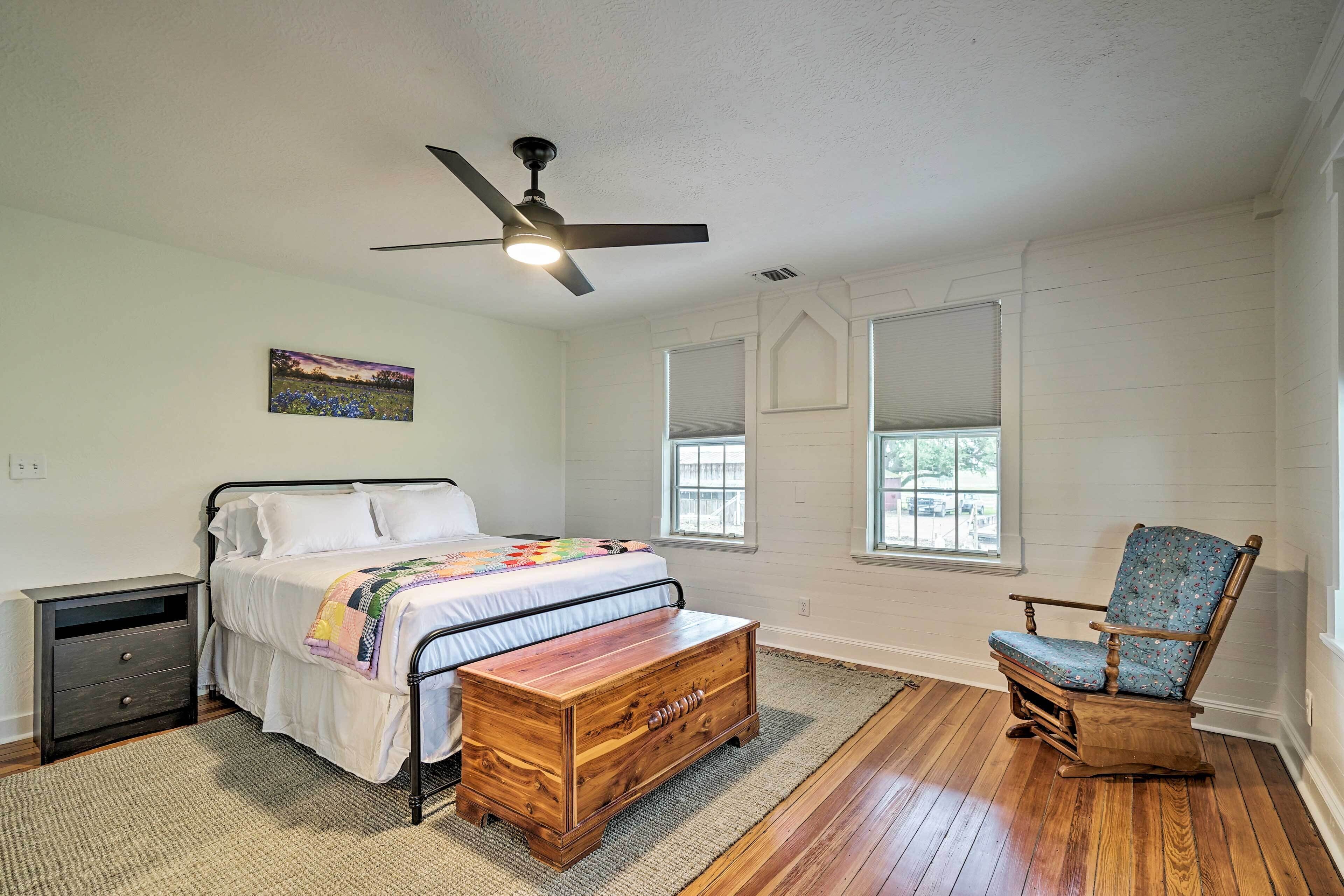 A bedroom with a bed, nightstand, wooden chest, rocking chair, and a ceiling fan.
