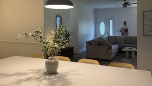Una cocina moderna con una isla central, un comedor con sillas de mimbre y una sala de estar con sofá y ventilador de techo.