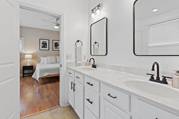 Un baño moderno con un espejo grande, muebles blancos y un tocador con lavabo.