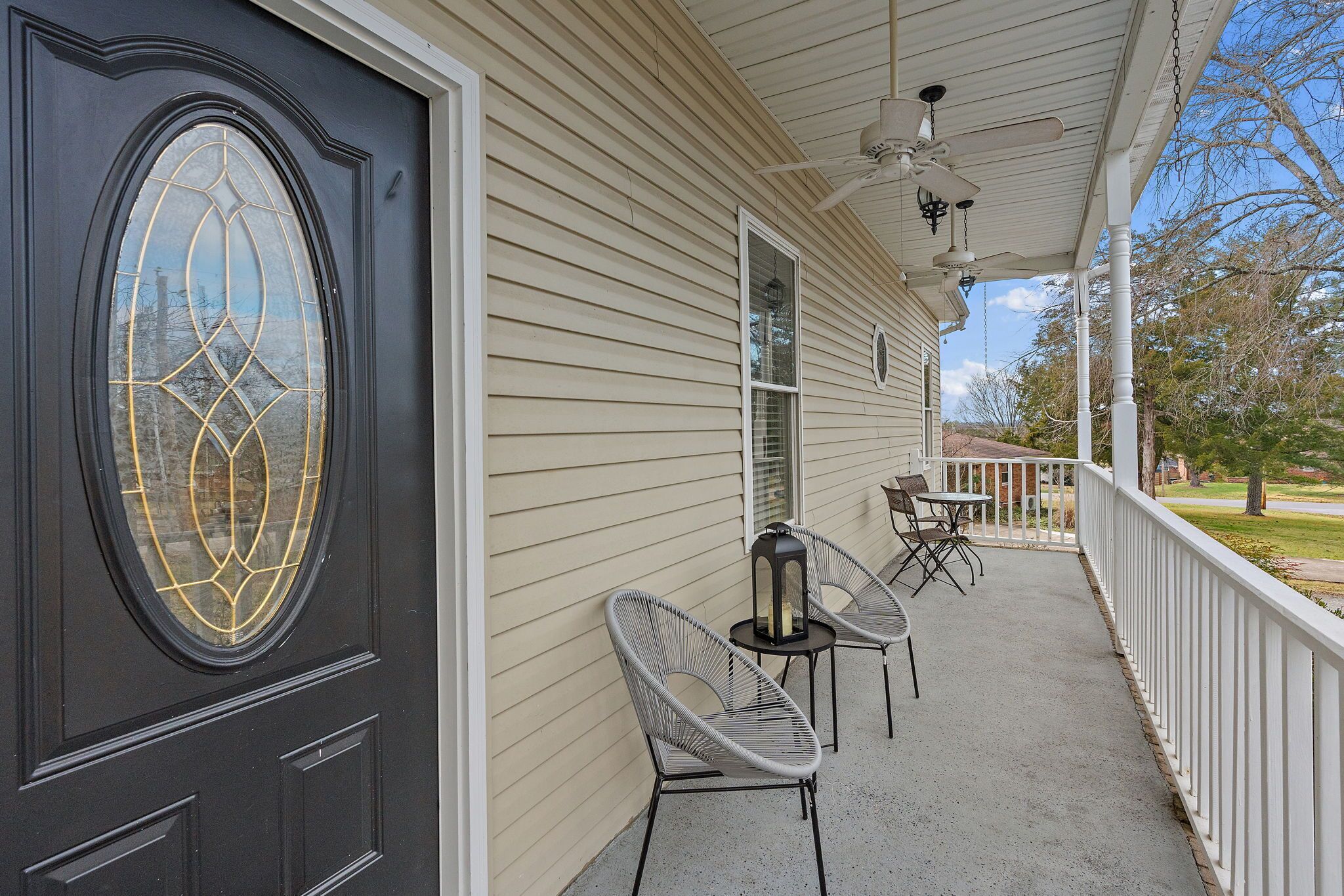 A house with a dark front door, beige siding, and a covered porch with two chairs and a table.