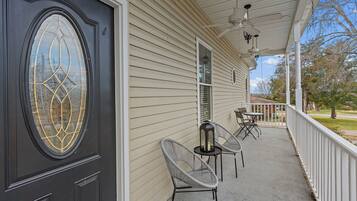 A house with a dark front door, beige siding, and a covered porch with two chairs and a table.