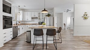 Una cocina moderna con armarios blancos, un refrigerador de acero inoxidable y una isla grande con taburetes de bar.