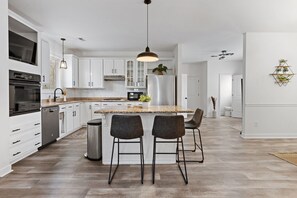 Een moderne keuken met witte kastjes, een roestvrijstalen koelkast en een groot kookeiland met barkrukken.