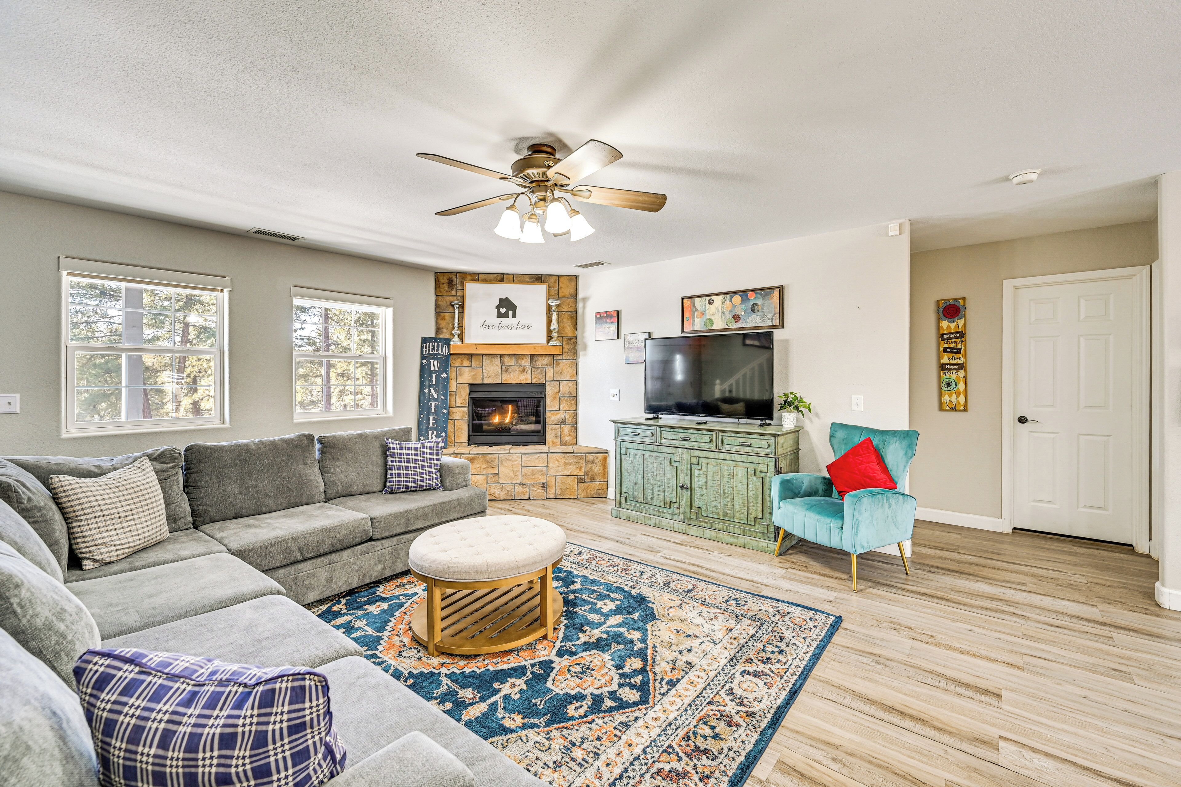 A living room with a sectional sofa, a fireplace, a television, and a teal armchair.