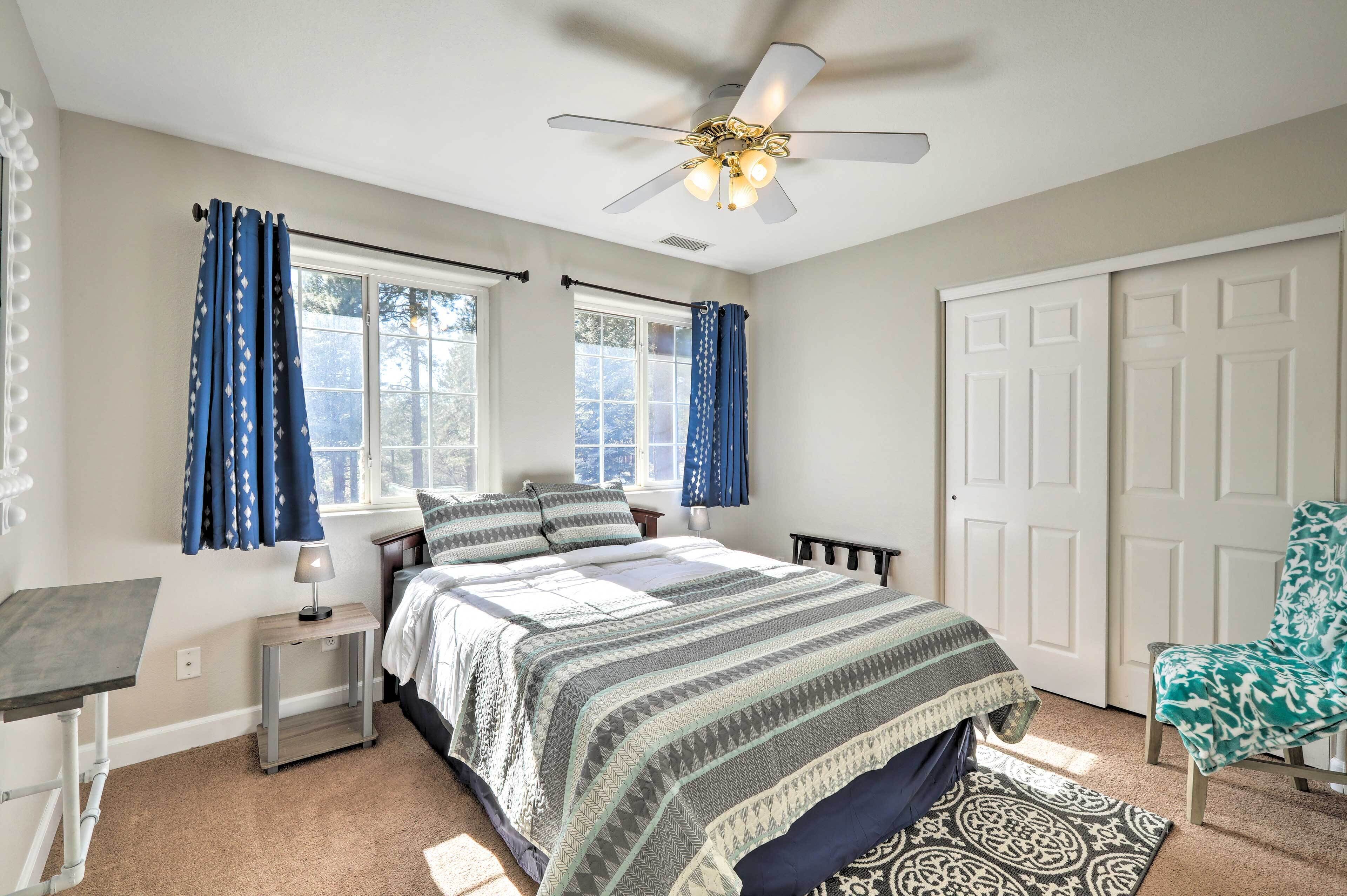 A bedroom with a bed, a desk, a chair, a ceiling fan, and a window with curtains.