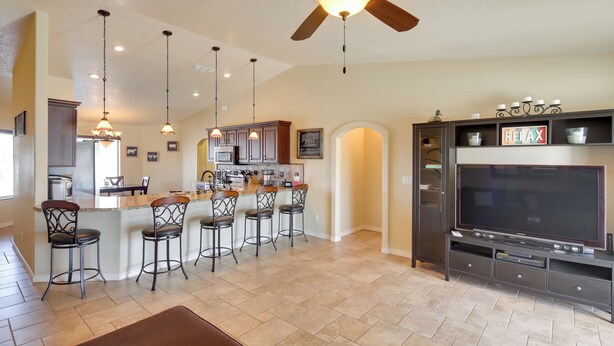 A spacious kitchen with a bar area, a large TV, and a ceiling fan.