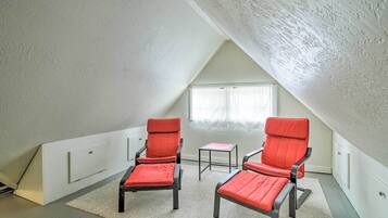 A small, triangular attic room with two red chairs, a small table, and a window.