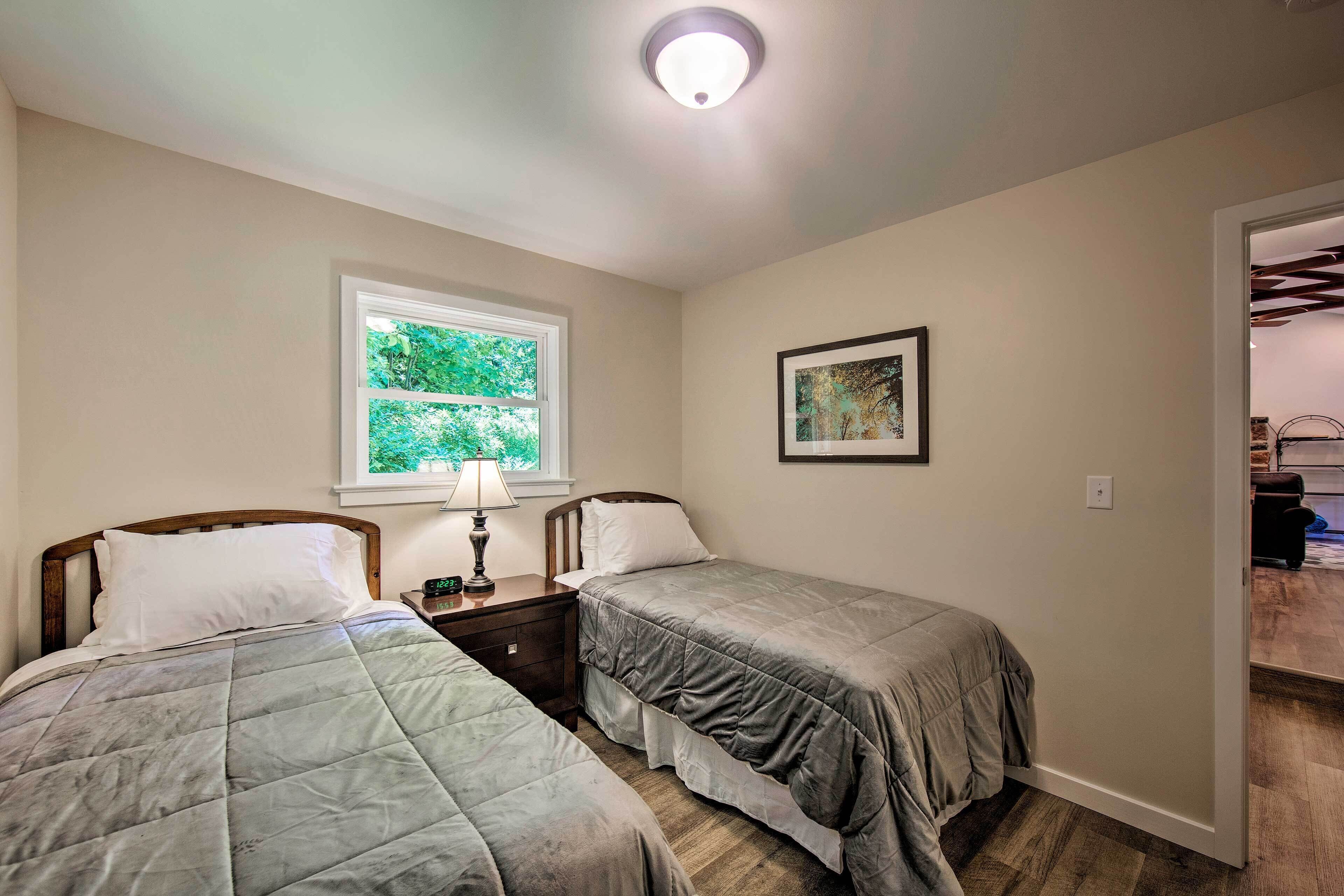 Un dormitorio con dos camas, una ventana que da a zonas verdes, un cuadro en la pared y una puerta que conduce a otra habitación.