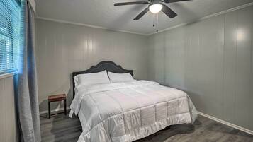 A bedroom with a bed, a nightstand, a ceiling fan, and a window with curtains.
