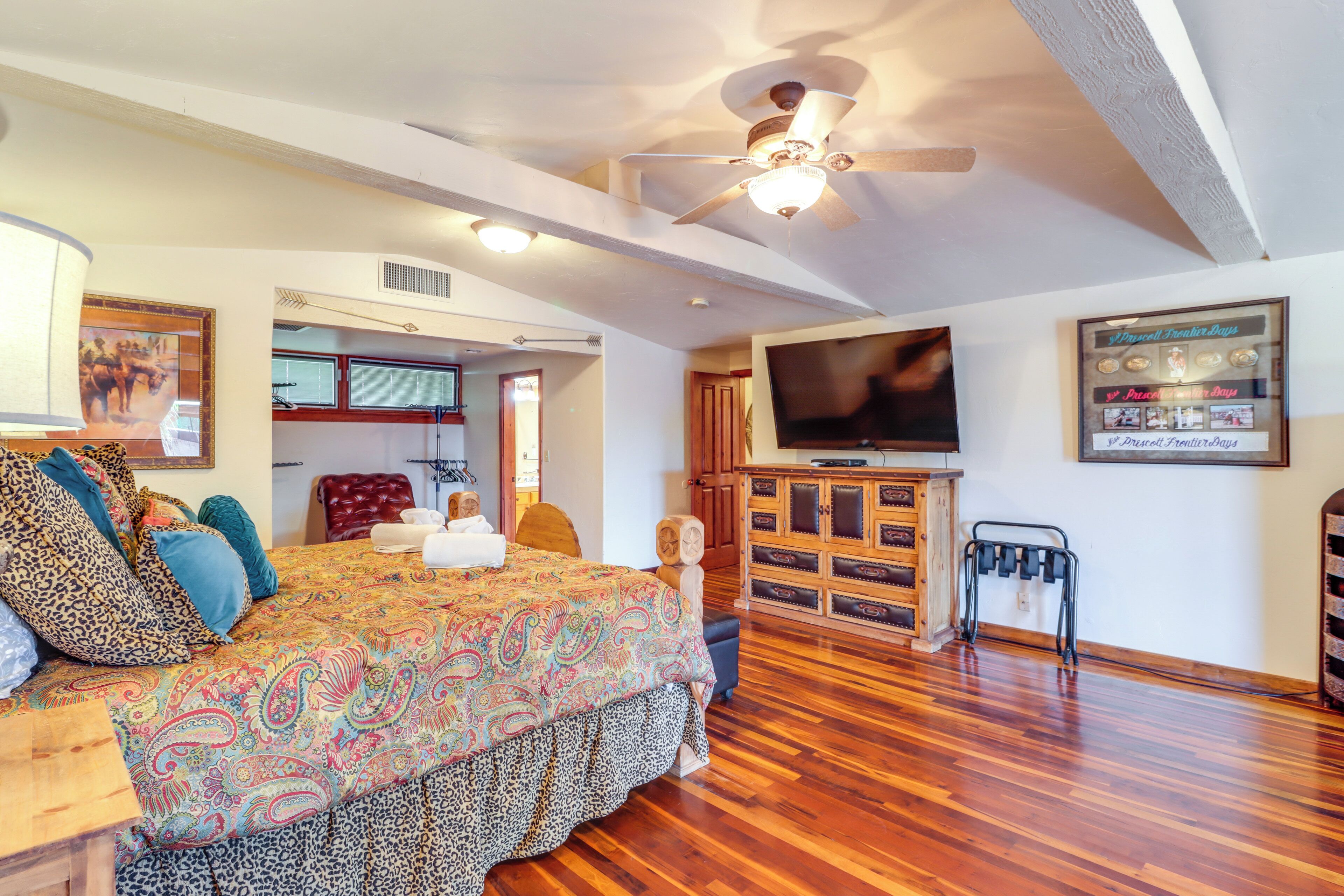 A spacious room with a large bed, wooden flooring, a ceiling fan, a television, and a wall-mounted cabinet.