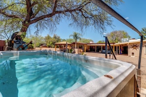 A hot tub area with a tree, outdoor seating, and a building with a sun motif. - Home Near Sabino Canyon: Hot Tub & Swim Spa Access (Tucson)