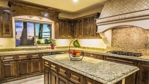 A kitchen with dark wood cabinets, a granite countertop, a window with a view, and a backsplash with a stone pattern. - Cabo Hacienda w/ Private Pool & Rooftop Terrace! (Cabo San Lucas)